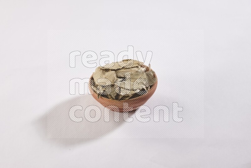 A wooden bowl filled with dried bay leaves on white flooring in different angles