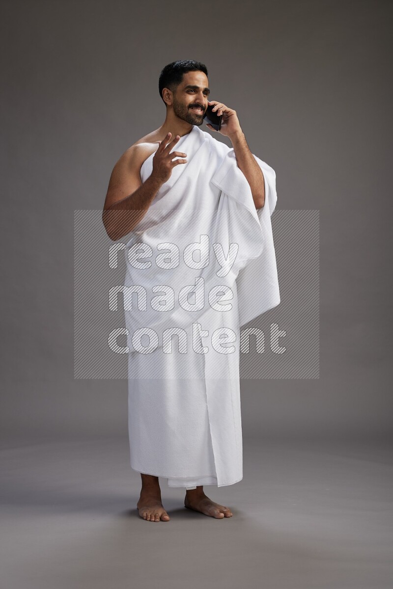 A man wearing Ehram Standing talking on phone on gray background