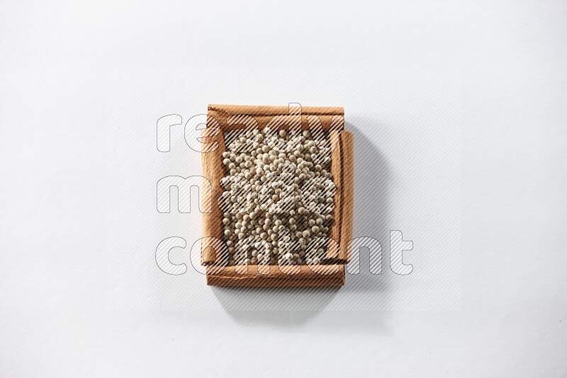 A single square of cinnamon sticks full of white pepper on white flooring
