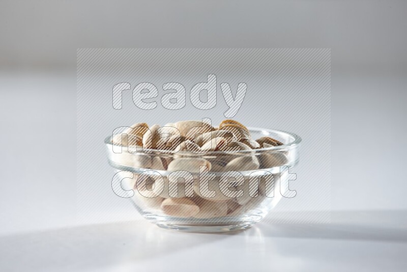 A glass bowl full of pistachios on a white background in different angles