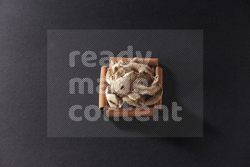 A single square of cinnamon sticks full of dried ginger on black flooring