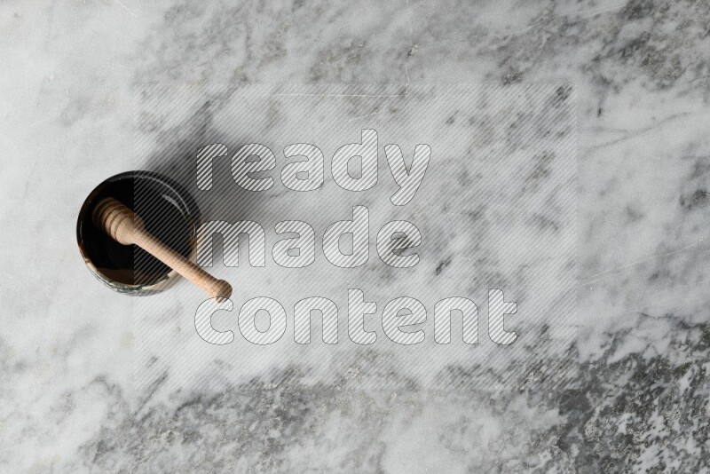 Multicolored pottery bowl with wooden honey dipper in it on grey marble background