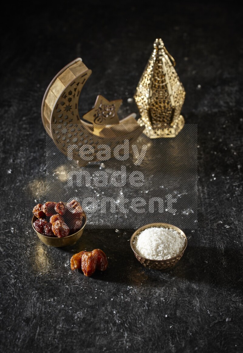 Dates in a metal bowl with desiccated coconuts beside golden lanterns in a dark setup