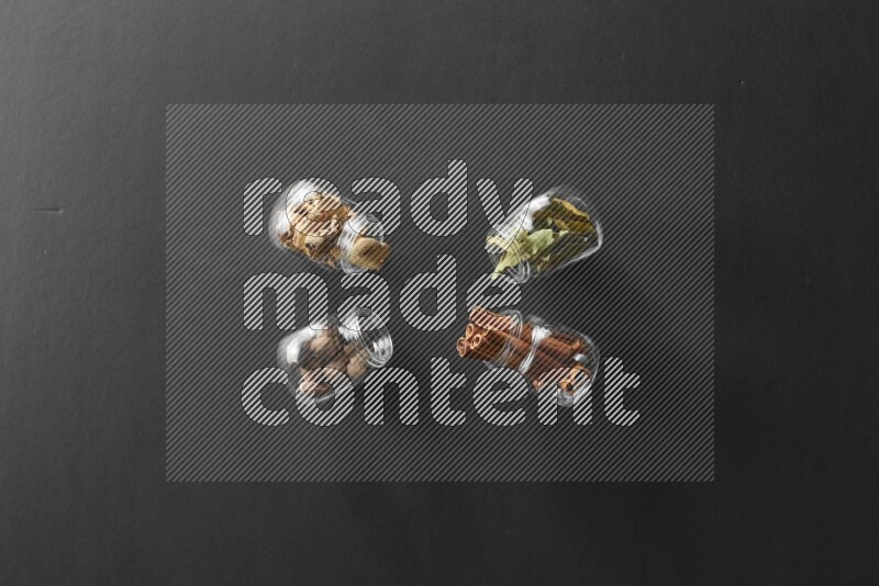 4 glass spice jars full of laurel bay leaves, ginger, cinnamon and nutmeg on black flooring