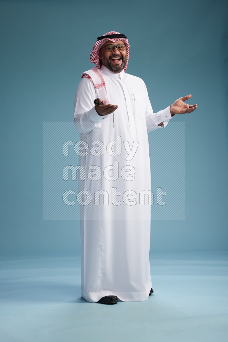 Saudi Man with shimag Standing Interacting with the camera on blue background