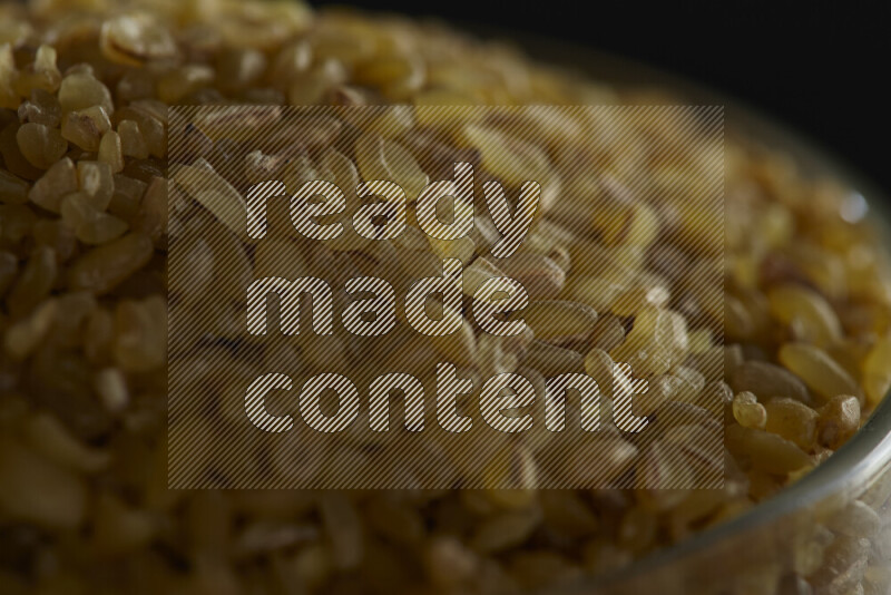 Coarse bulgur in a glass jar on black background