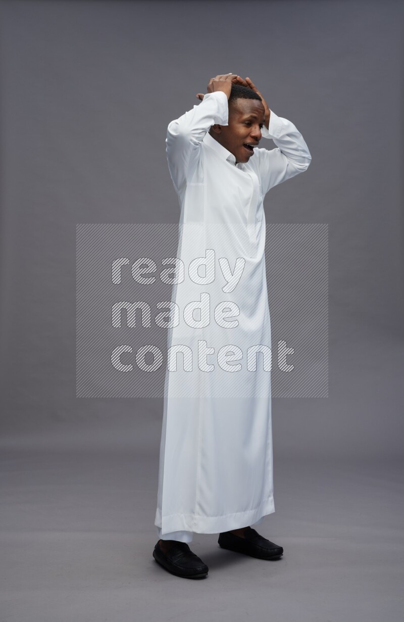 Saudi man wearing thob standing hands behind head on gray background