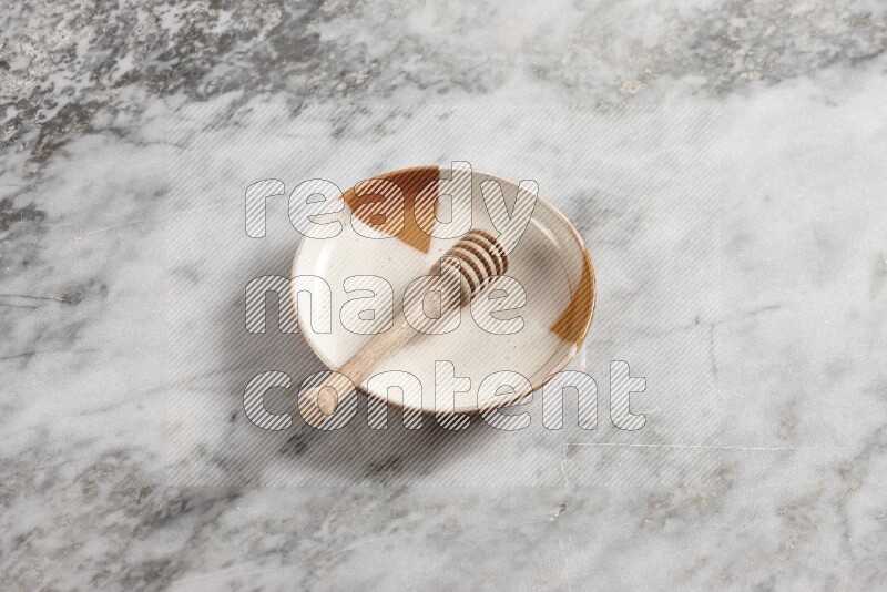 Multicolored pottery plate with wooden honey dipper in it on grey marble background
