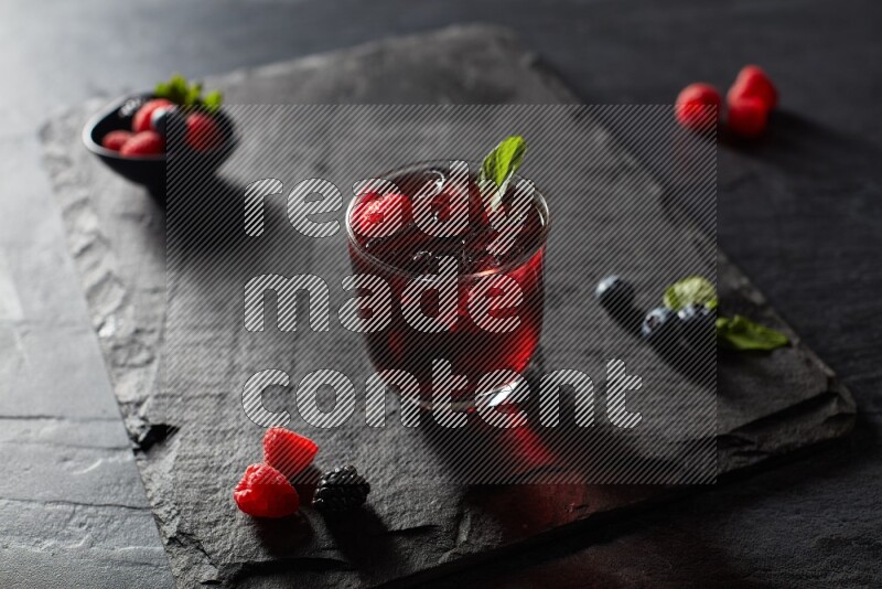 A glass of mixed berries juice with mint leaves on black background