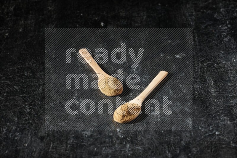 Wooden spoons full of allspice powder on a textured black flooring