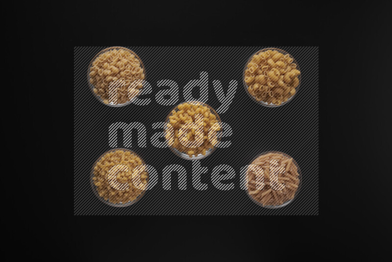 Different pasta types in 5 glass bowls on black background