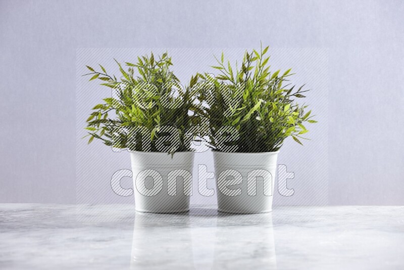 Two green artificial plants in white pot on grey marble background