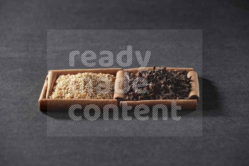 مربعان من أعواد القرفة ممتلئان ببذور السمسم والقرنفل علي خلفية سوداء