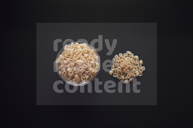 Shells pasta in a glass bowl on black background