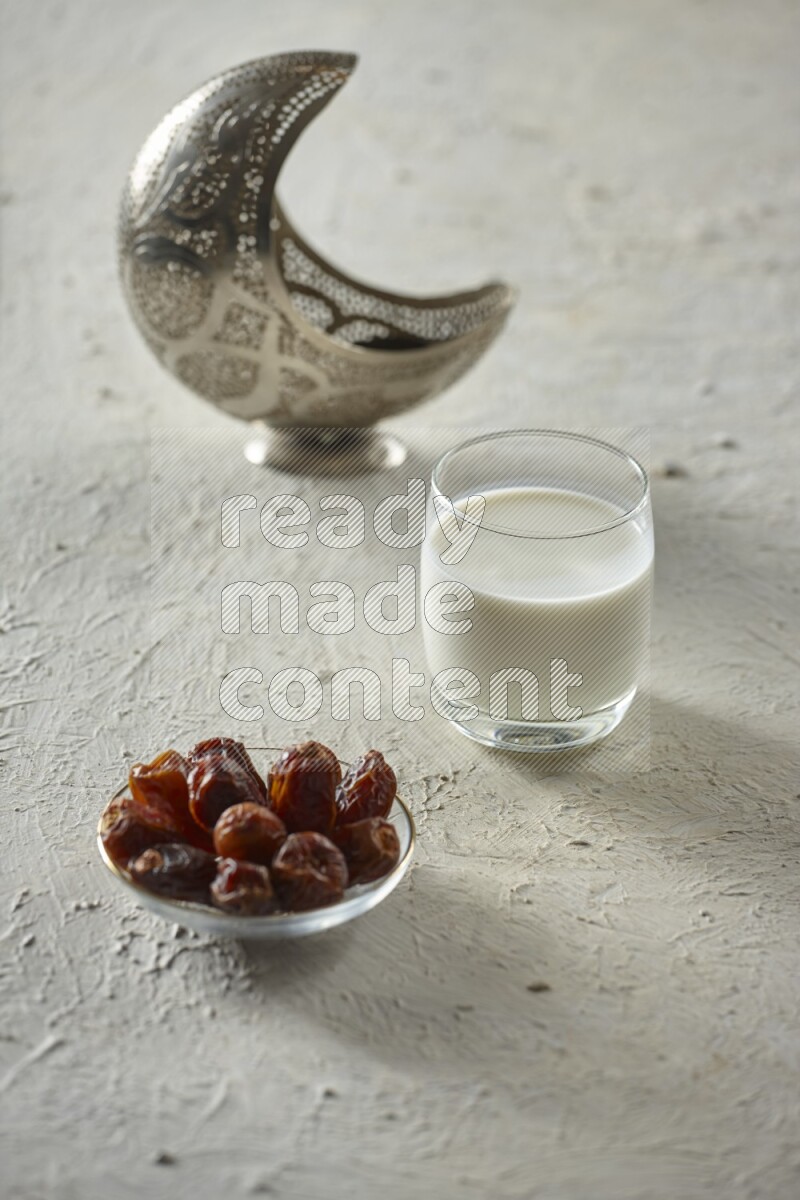 A silver lantern with different drinks, dates, nuts, prayer beads and quran on textured white background