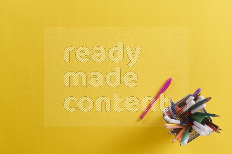 Pens, pencils and school supplies in a metal pen holder on yellow background