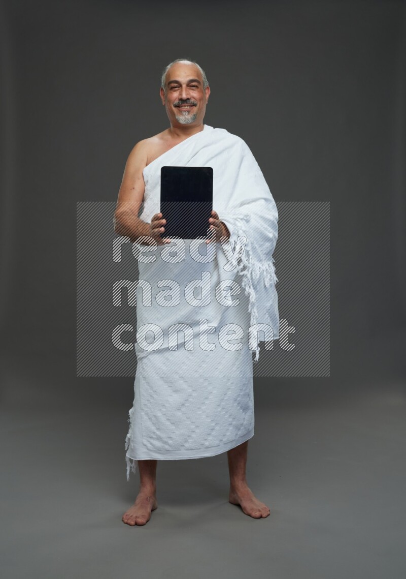 A man wearing Ehram Standing working on tablet on gray background