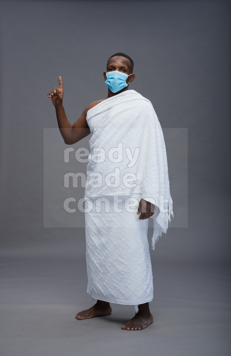 A man wearing Ehram with face mask Standing Interacting with the camera on gray background