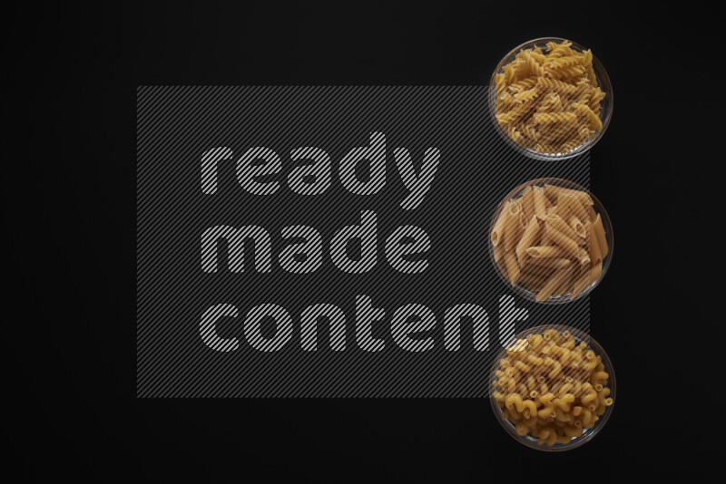 Different pasta types in 3 glass bowls on black background