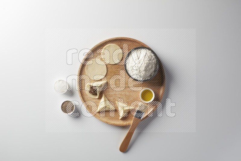 two closed sambosas and one open sambosa filled with meat while flour, salt, black pepper and oil with oil brush aside in a wooden dish on a white background