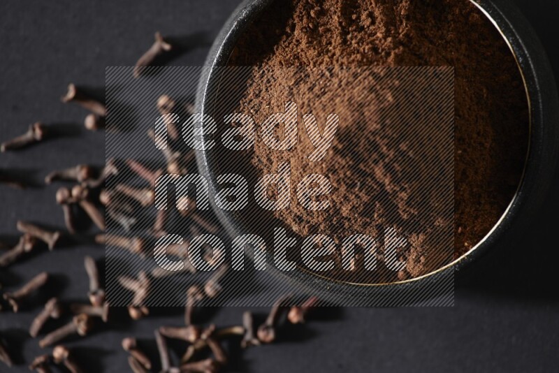 وعاء فخاري أسود ممتلئ ببودرة القرنفل وحبوب القرنفل على خلفية سوداء