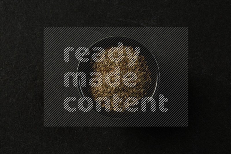 black pottery round sauce bowl filled with herbs on grey textured countertop