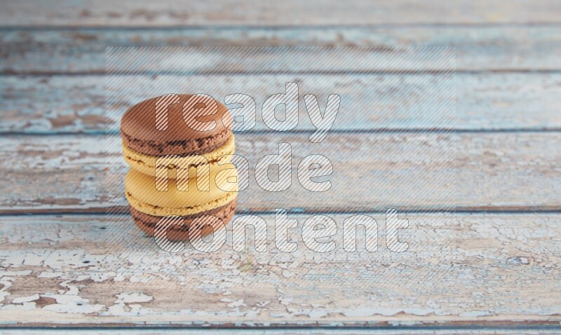 45º Shot of two Yellow and Brown Chai Latte macarons on light blue wooden background