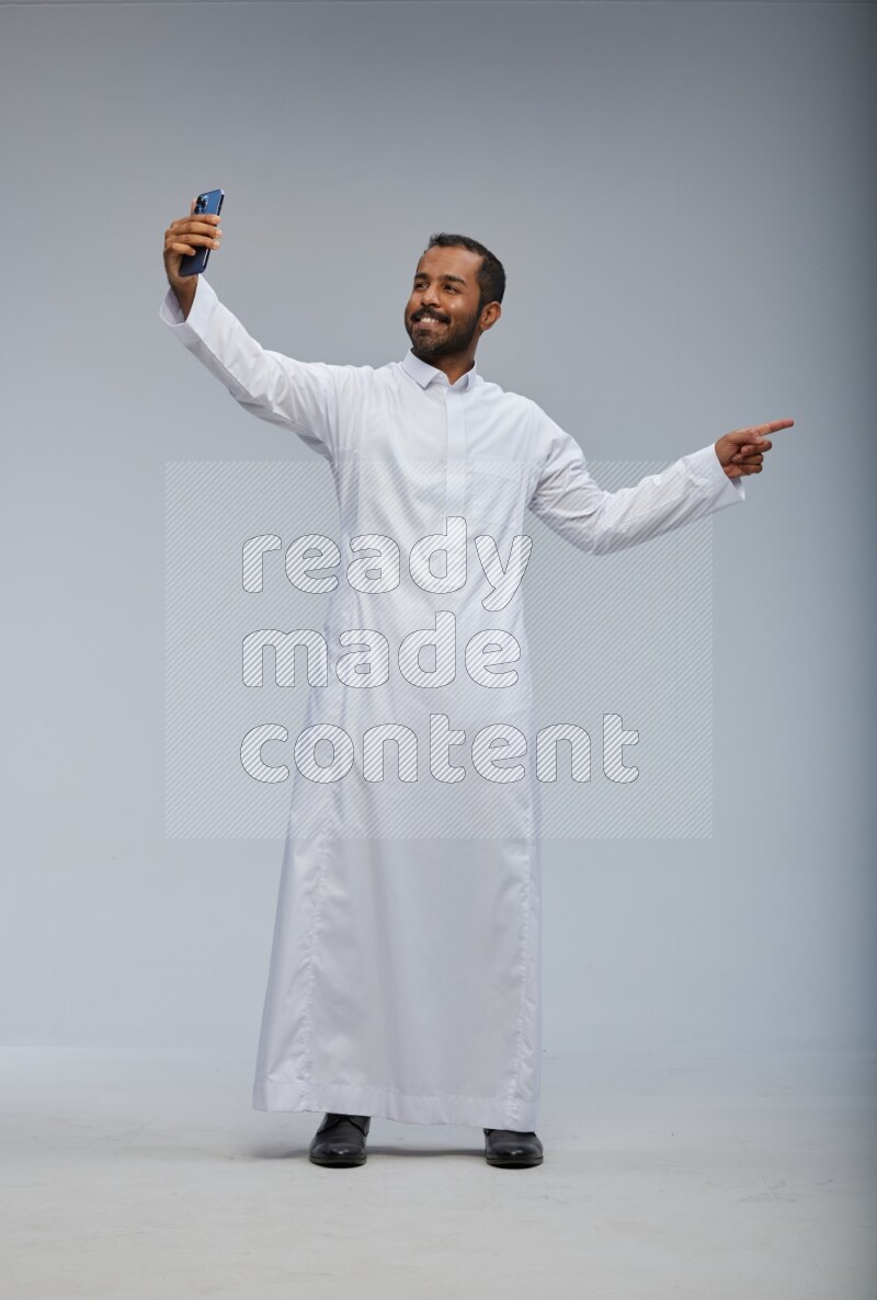 Saudi man wearing Thob standing taking selfie on Gray background
