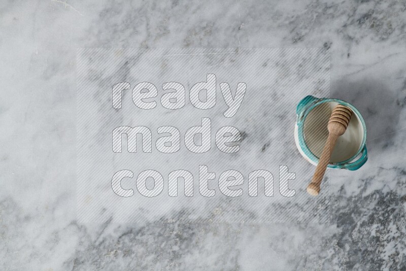 Multicolored pottery bowl with wooden honey dipper in it on grey marble background