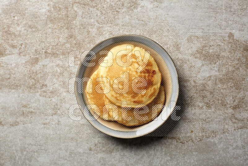 Three stacked plain pancakes in a bicolor plate on beige background