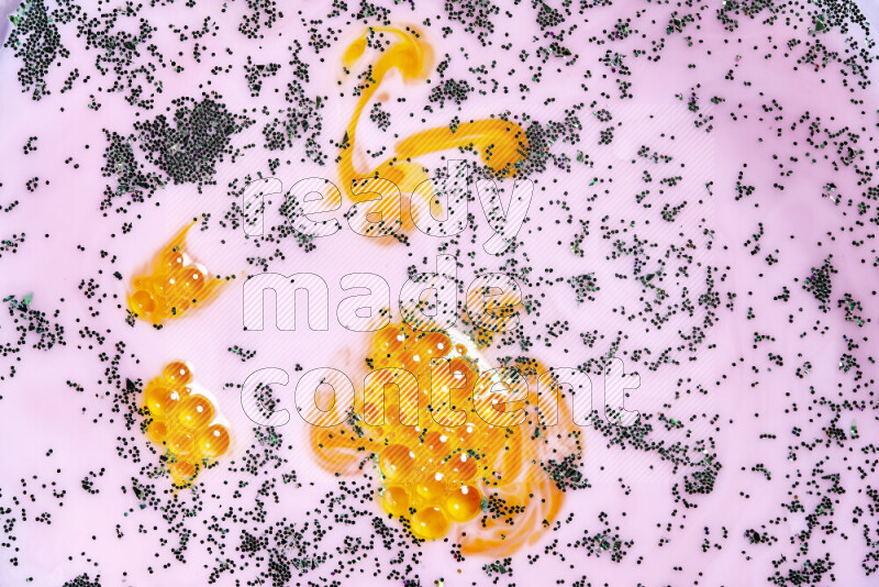 A close-up of sparkling green glitter scattered on swirling yellow and pink background