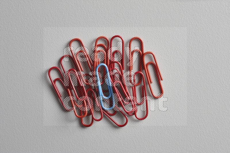 A bunch of red paper clips with a different colored paper clip in the center on grey background