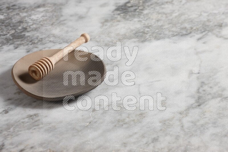 Multicolored pottery plate with wooden honey dipper in it on grey marble background