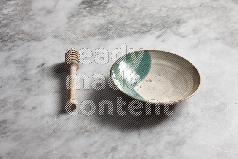 Multicolored pottery plate with wooden honey dipper on the side on grey marble background