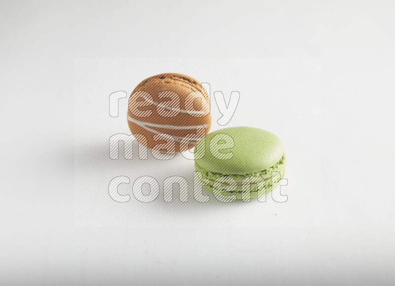 45º Shot of of two assorted Brown Irish Cream, and Green Pistachio macarons on white background