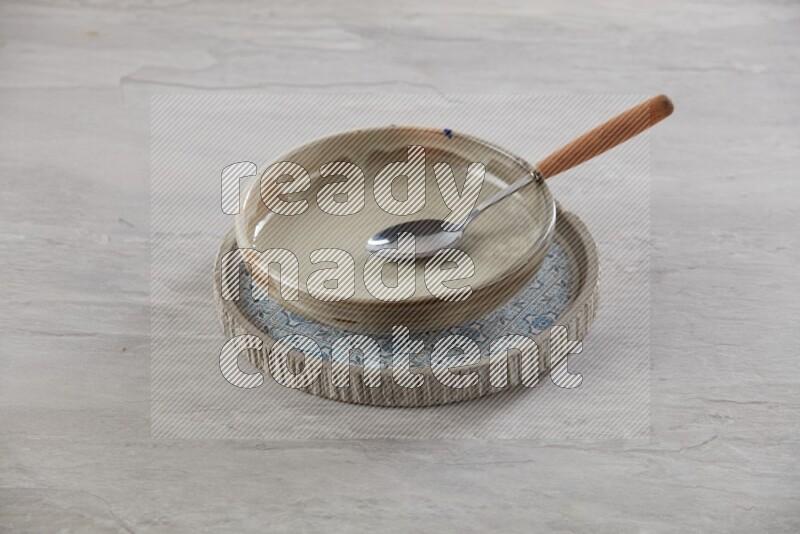 multi color pottery round dish on top of multi color round ceramic plate and spoon, on grey textured countertop