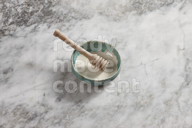 Multicolored pottery bowl with wooden honey dipper in it on grey marble background