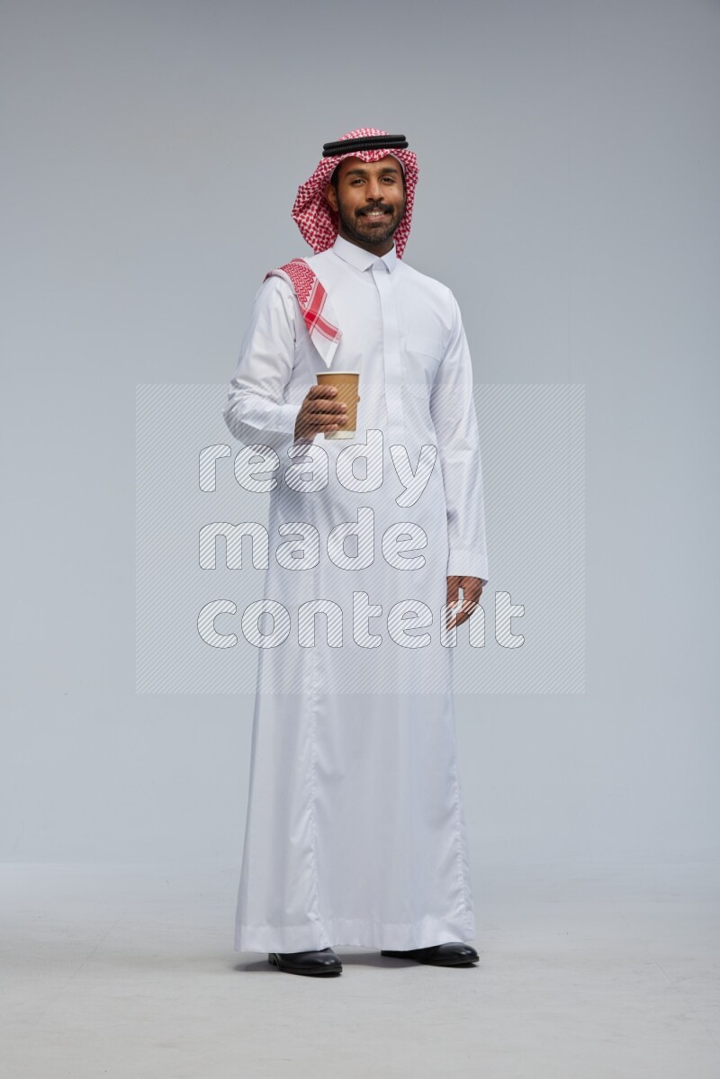 Saudi man Wearing Thob and shomag standing holding paper cup on Gray background