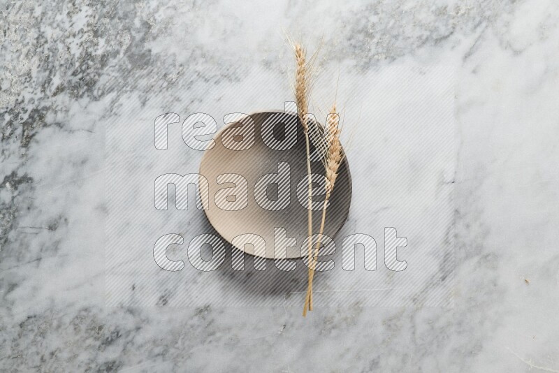 Wheat stalks on multicolored pottery plate on grey marble background
