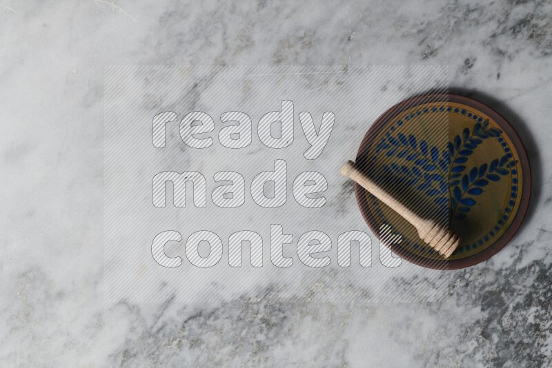 Decorative pottery plate with wooden honey dipper in it on grey marble background