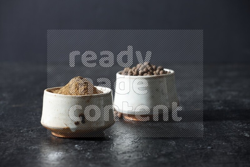 2 beige bowls, one full of allspice powder and the other full of whole balls on a textured black flooring