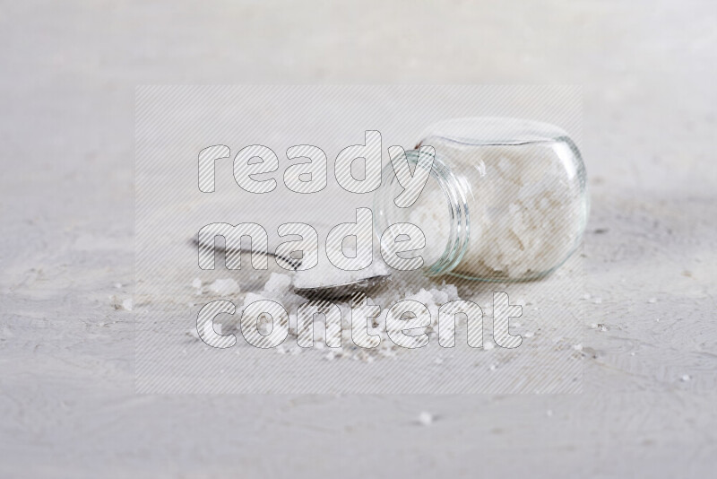 A glass jar full of coarse sea salt crystals on white background