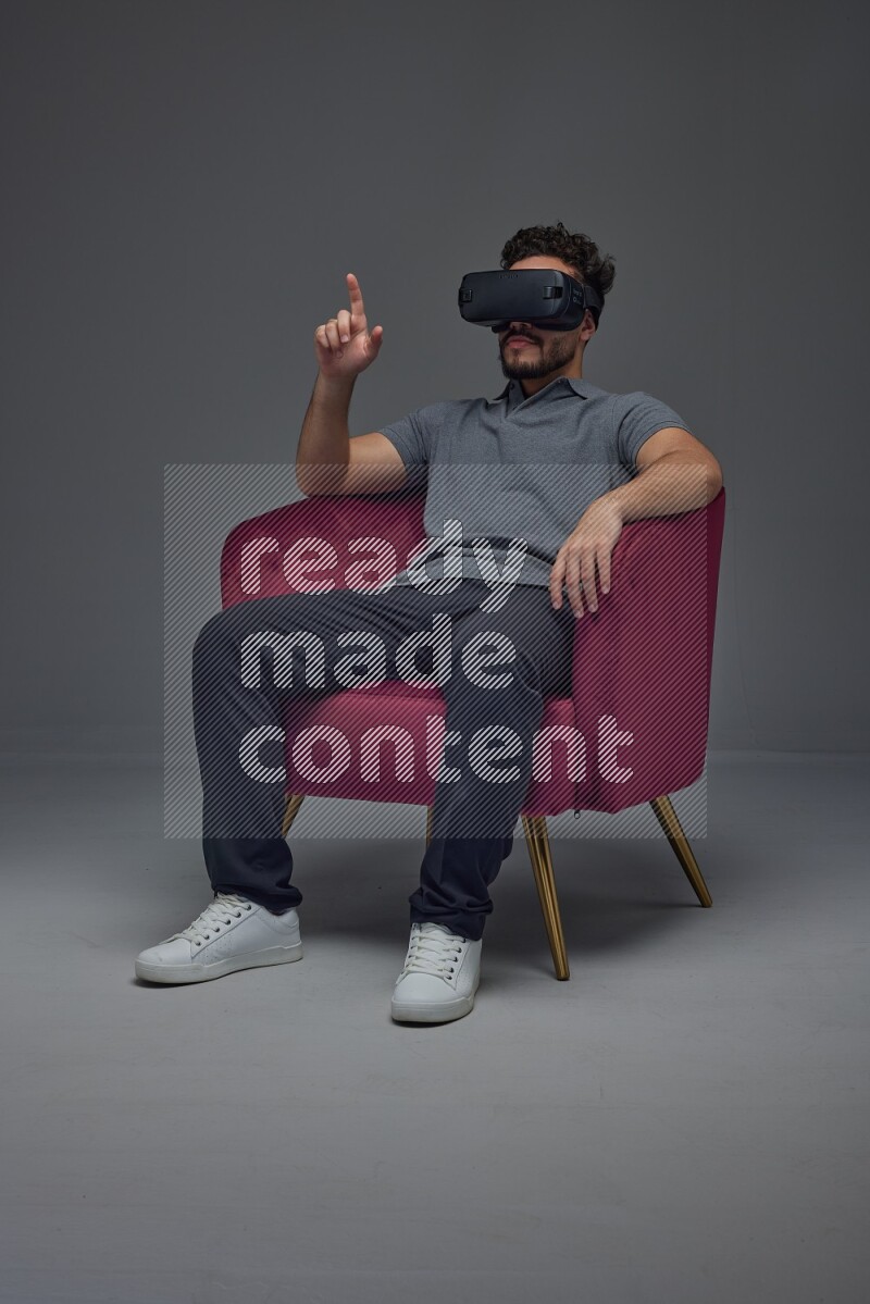 A man wearing casual and wearing VR while sitting on a burgundy chair eye level on a gray background