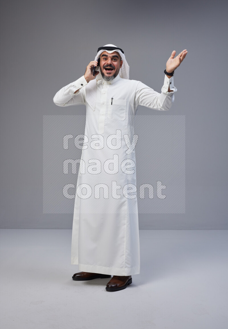 Saudi man Wearing Thob and white Shomag standing talking on phone on Gray background