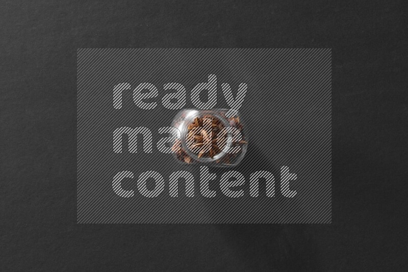 A glass spice jar full of star anise on black flooring
