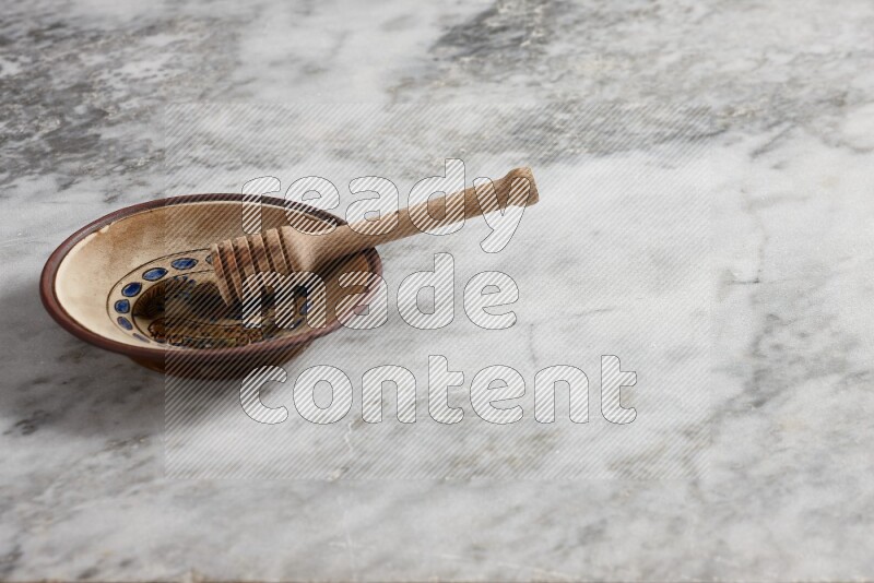 Decorative pottery plate with wooden honey dipper in it on grey marble background