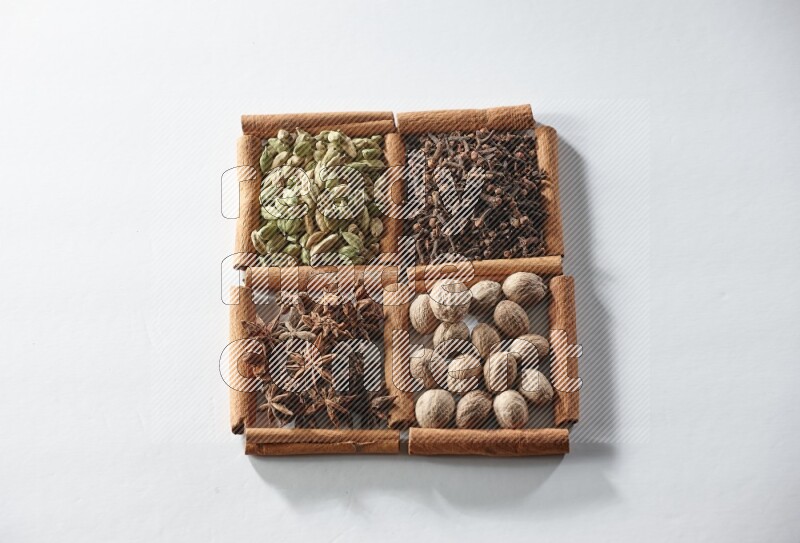 4 مربعات من أعواد القرفة ممتلئة بالهيل واليانسون والقرنفل وجوزة الطيب على أرضية بيضاء