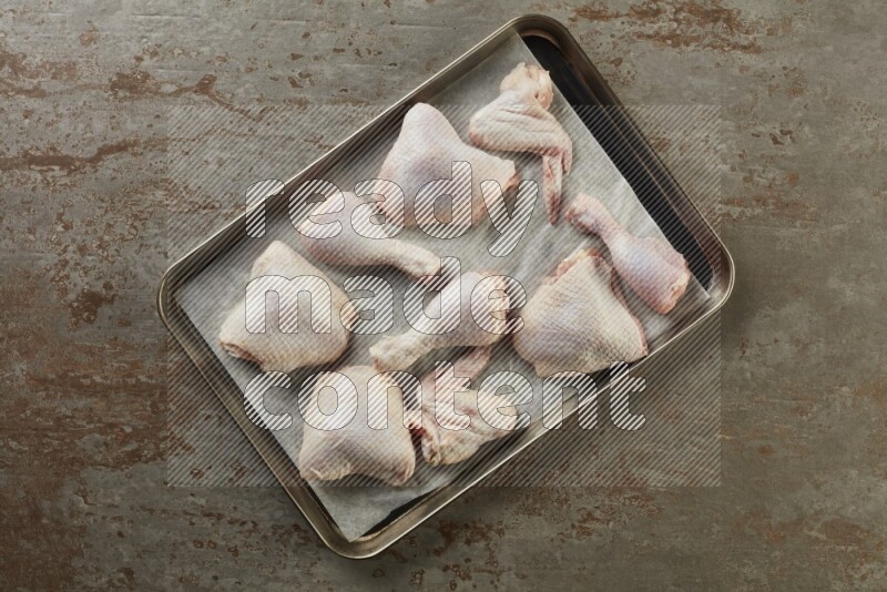 Mixed fresh chicken pieces in an oven tray on a textured rustic background