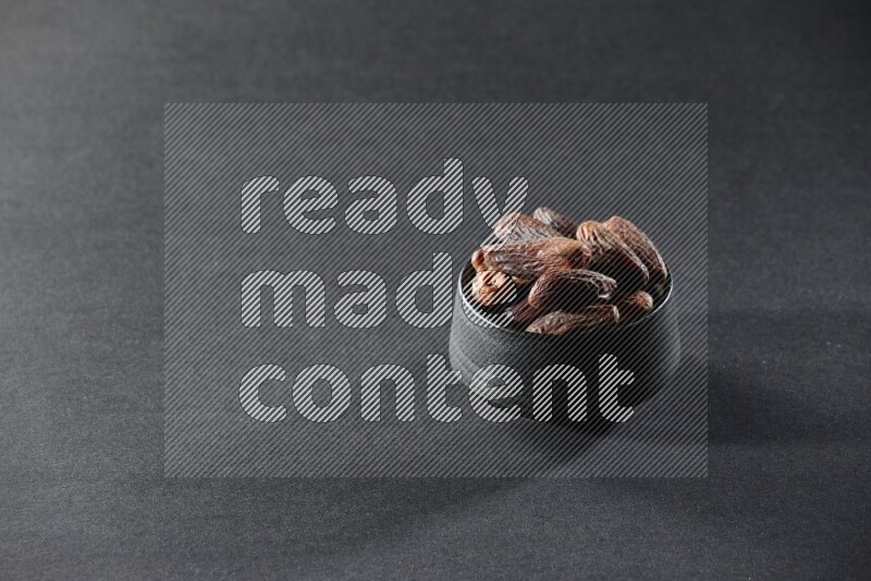 A black pottery bowl full of dried dates on a black background in different angles