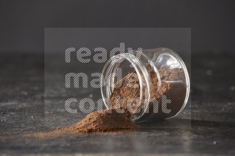 A flipped glass jar full of cloves powder on a textured black flooring